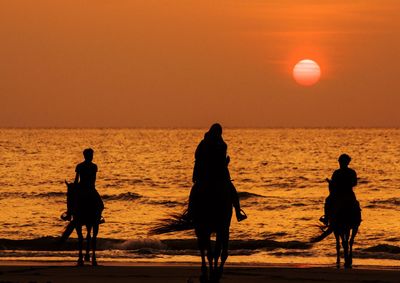 Silhouette people on beach against sky during sunset