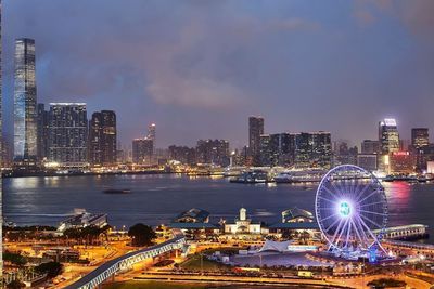 Illuminated city by river against sky at night