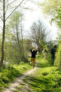 Rear view of person with arms raised running on trail