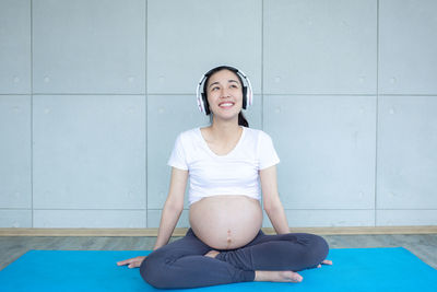 Smiling young woman sitting against wall