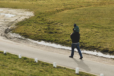 Father carrying son on shoulders while walking on road