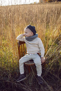 Fashionable boy child sitting on a chair in autumn on the field