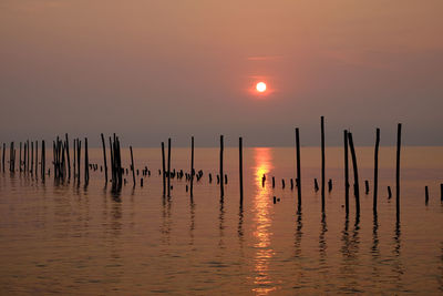 Silhouette wooden posts in sea against sky during sunset