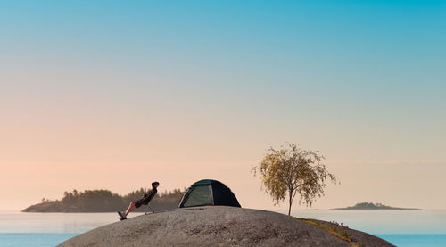 Side view of man resting by tent against sky during sunset