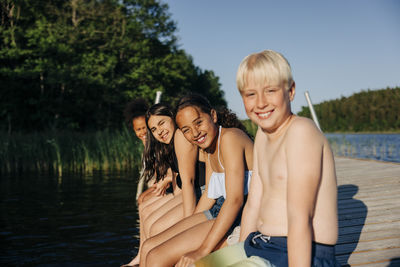 Portrait of smiling kids sitting together on jetty near lake at summer camp