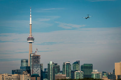 View of urban skylines with communication tower and airplane flying in sky