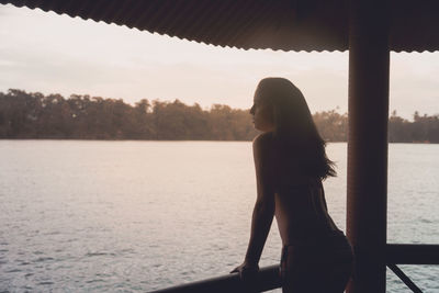 Thoughtful man standing in gazebo against lake during sunset