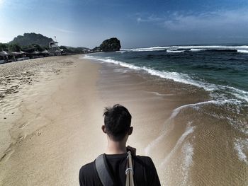 Rear view of man standing on wet beach