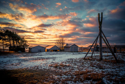 Snow covered landscape against cloudy sky at sunset