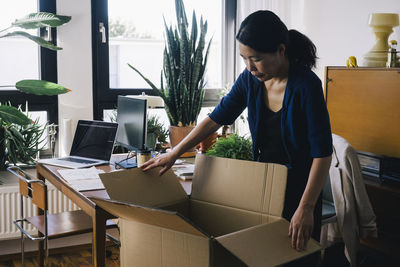 Mature female architect opening cardboard box at home office