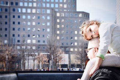 Grandfather carrying granddaughter on shoulders against building