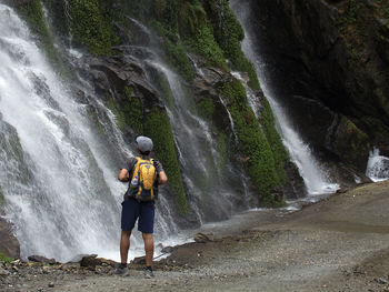 Full length of man standing on rock against waterfall