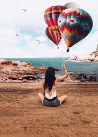 Rear view of woman flying over beach against sky