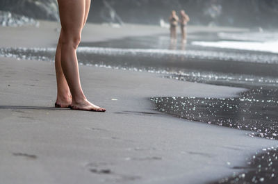 Low section of woman standing on wet shore