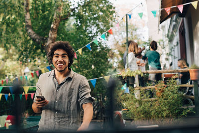 Portrait of young man holding mobile phone while standing in backyard