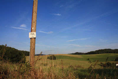 Placard on wooden post at field against sky