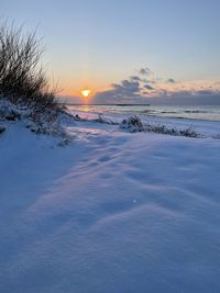 Scenic view of snow covered land against sky during sunset