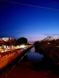 River by illuminated city against clear sky at dusk