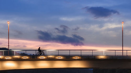 Silhouette bridge over sea against sky at sunset