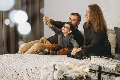 Family with child playing near christmas tree. child unpacking gifts, parents enjoy christmas tree