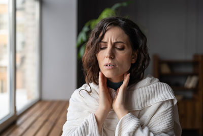 Upset sick woman standing at home touching swollen glands, suffering from angina or tonsillitis