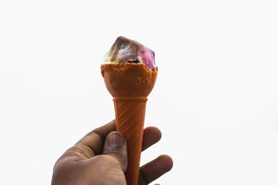 Close-up of hand holding ice cream against white background