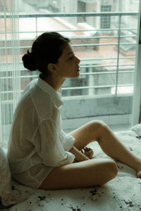 Side view of woman looking away while sitting on window