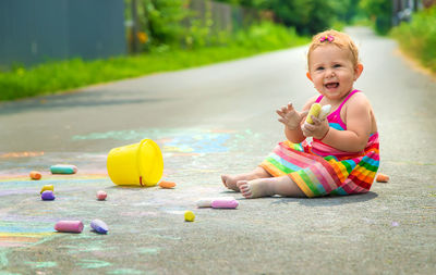 Cute baby girl playing with toy sitting on road