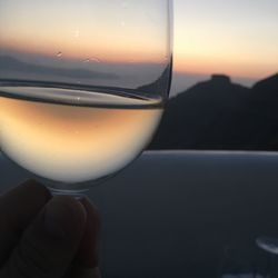 Close-up of hand holding wineglass against sunset