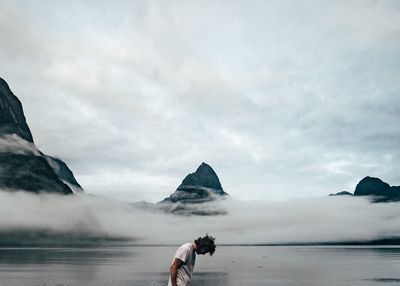 Side view of man at lakeshore against cloudy sky