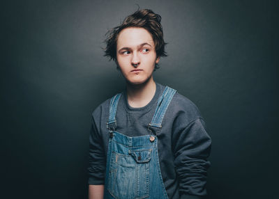 Young man wearing overalls while looking sideways over gray background