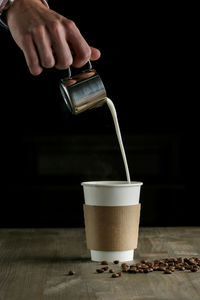 Cropped image of hand pouring milk in coffee glass 