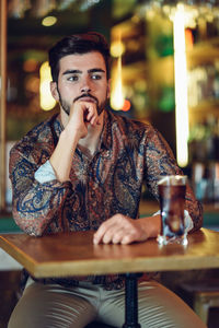 Thoughtful young man sitting by drink on table at restaurant