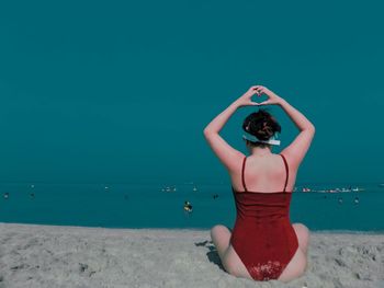 Rear view of woman standing on beach against clear blue sky