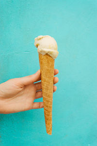 Cropped image of hand holding ice cream cone against blue wall