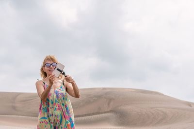 Blonde woman in dress doing a selfie with the mobile in the middle of dunes
