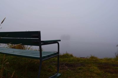 Empty bench by sea against sky