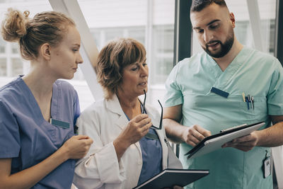 Mature female physician holding eyeglasses while discussing with hospital staff
