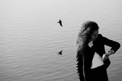 Woman checking time with bird flying over lake