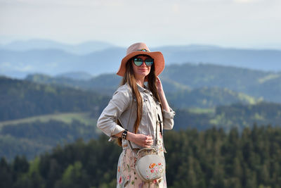 Woman wearing hat and sunglasses while standing against mountain