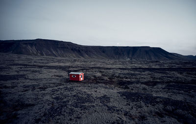 Small red house in dark dry terrain surrounded by hills