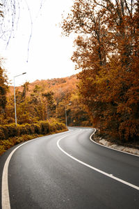 Country road amidst trees against sky during autumn