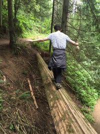 Rear view of man standing on tree trunk in forest