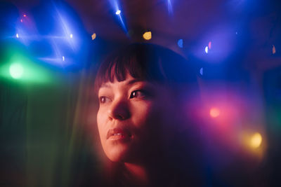 Thoughtful young woman looking away amidst multi colored lights in restaurant