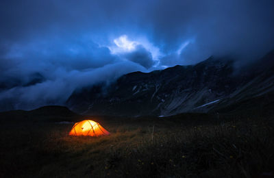 Illuminated tent on field against cloudy sky at night