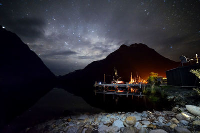 Illuminated pier on lake against star field