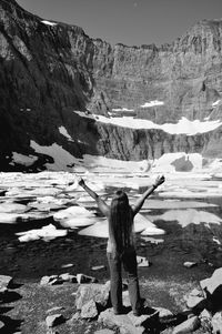 Rear view of mature woman with arms raised standing on rock by lake during winter