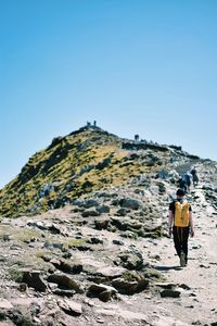 Rear view of man climbing mountain against clear sky