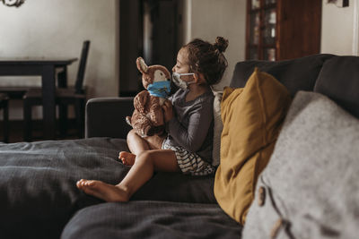 Side view of preschool age girl with mask on cuddling masked doll