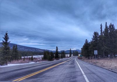 Empty road along trees and against sky